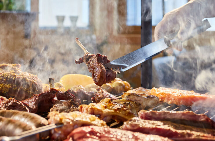 Das Fleisch wird auf den Grill gelegt, Rippchen, Würste, Hühnchen. Es handelt sich um ein Grillgericht. Verschiedene Portionen Fleisch werden gegart und den Gästen serviert.