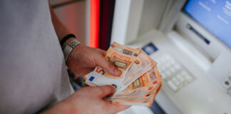 Junge Männerhände halten mehrere 50-Euro-Scheine fest. Der Mann steht offenbar vor einem Geldautomaten und zählt sein Geld, welches er gerade abgeholt hat, nach. An seiner rechten Hand befindet sich eine Uhr.