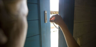 Jemand verschließt seine Tür von innen mit einem Vorhängeschloss, um sich vor Einbrechern oder anderen Eindringlingen zu schützen. Eine gemeine Methode mit Säure an Haustüren vorzugehen ist nämlich im Umlauf.