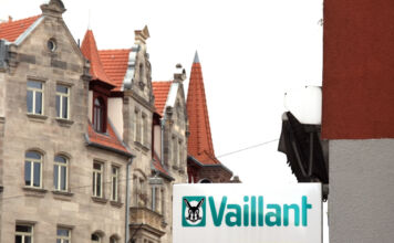 Eine Straße mit historisch anmutenden Gebäuden unter bedecktem Himmel. An einem der Hauswände hängt das Schild der Firma Vaillant in den klassischen Logofarben des Unternehmens.