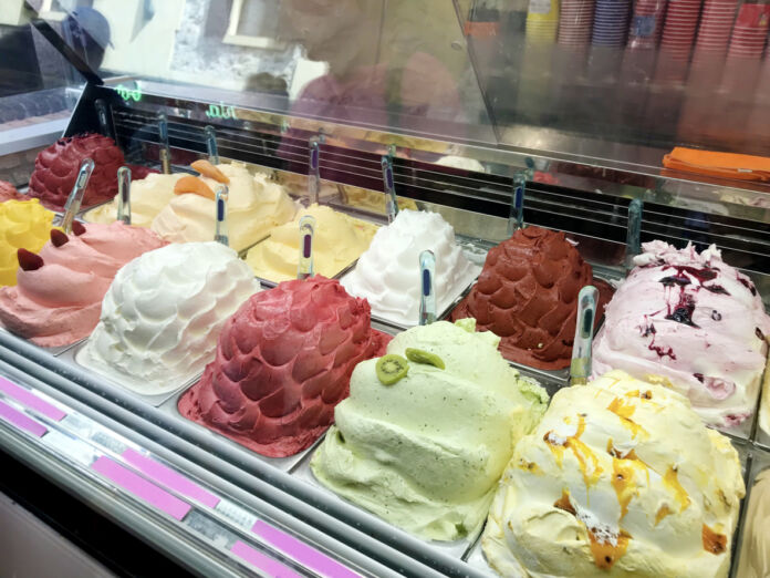 Eine Verkaufstheke in einem Eiscafé oder einer Eisdiele mit verschiedenen Eissorten wie Vanilleeis, Milcheis, Schokoladeneis, Fruchteis und Sorbet in unterschiedlichen appetitlichen Farben.