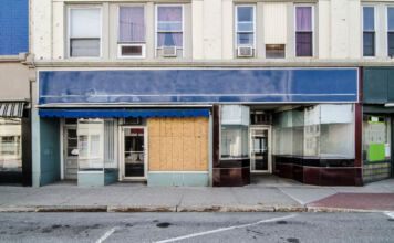 Ein Ladengeschäft in einer Stadt sieht verlassen aus, weil alle Fenster mit Rollläden geschlossen wurden. Die Straße ist verlassen und kein Mensch ist im Geschäft.