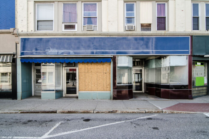Ein Ladengeschäft in einer Stadt sieht verlassen aus, weil alle Fenster mit Rollläden geschlossen wurden. Die Straße ist verlassen und kein Mensch ist im Geschäft.