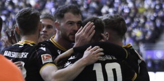 Die Spieler des Karlsruher SC liegen sich nach einem Spiel in den Armen. Sie umarmen sich vor Freude und machen zufriedene Gesichter.