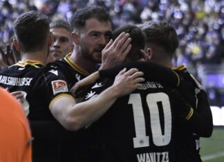 Die Spieler des Karlsruher SC liegen sich nach einem Spiel in den Armen. Sie umarmen sich vor Freude und machen zufriedene Gesichter.