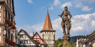 Eine Statue von einem Mann mit Schild steht in einer charmanten Altstadt vor Fachwerkhäusern und begeistern Touristen, die in der Gegend wandern gehen