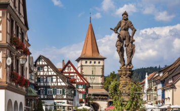 Eine Statue von einem Mann mit Schild steht in einer charmanten Altstadt vor Fachwerkhäusern und begeistern Touristen, die in der Gegend wandern gehen
