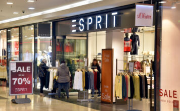 Eine Esprit-Filiale befindet sich in einem Einkaufszentrum. Einige Menschen schlendern an dem Eingang vorbei, andere gehen in den Laden. Vor dem Eingang weist ein Schild auf einen Schlussverkauf mit einer Ersparnis von bis zu 70% hin.