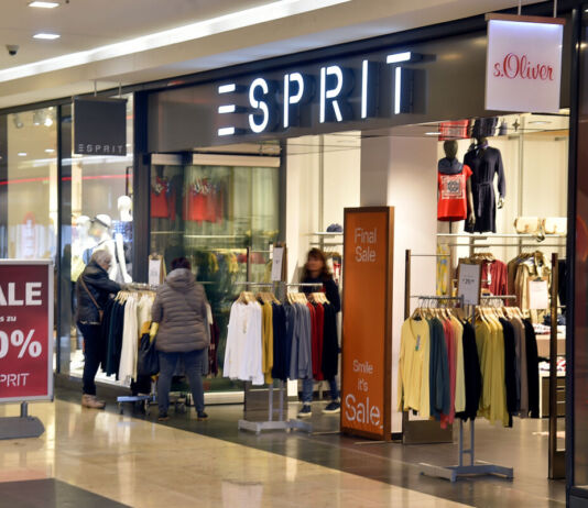 Eine Esprit-Filiale befindet sich in einem Einkaufszentrum. Einige Menschen schlendern an dem Eingang vorbei, andere gehen in den Laden. Vor dem Eingang weist ein Schild auf einen Schlussverkauf mit einer Ersparnis von bis zu 70% hin.
