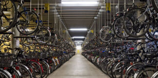 Große beleuchtete Lagerhalle mit mehreren Hundert abgestellten Fahrrädern in einer Reihe links und rechts. Darüber hängen und parken Fahrräder in zweiter Reihe.