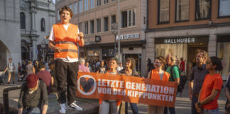Die Klimaaktivisten der letzten Generation sind auf einer Demo oder einem Protestmarsch. Sie halten bei der Aktion ein Transparent hoch mit der Aufschrift: "Letzte Generation vor den Kipppunkten".