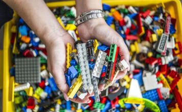 Die Hände eines Mannes greifen in eine volle Kiste mit Legosteinen, beziehungsweise in bunte Bausteine, die mit Steckverbindungen zusammengefügt werden können.