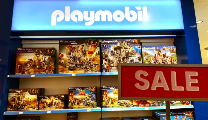 Verschiedene Playmobil Spielwaren-Packungen stehen in einem Regal. Davor steht ein Schild mit der Aufschrift 