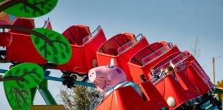 Eine rote Achterbahn mit einer rosa Peppa Pig Figur im ersten Wagon fährt auf blauen Schienen. Die Achterbahn ist neu und gehört zu einem Freizeitpark in Deutschland