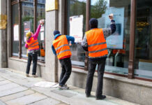 Die Letzte Generation wieder in Aktion! Aktivisten bekleben mehrere Bankfilialen mit Plakaten und Tapetenkleister. Dabei tragen sie leuchtende Warnwesten und wetterfeste Kleidung.