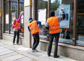 Die Letzte Generation wieder in Aktion! Aktivisten bekleben mehrere Bankfilialen mit Plakaten und Tapetenkleister. Dabei tragen sie leuchtende Warnwesten und wetterfeste Kleidung.