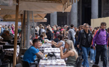 Viele Touristen sitzen sich an verschiedenen Tischen in Italien gegenüber und unterhalten sich während sie Essen und Getränke genießen