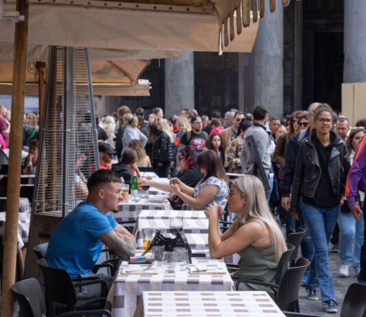 Viele Touristen sitzen sich an verschiedenen Tischen in Italien gegenüber und unterhalten sich während sie Essen und Getränke genießen
