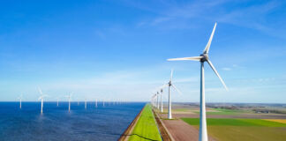 Mehrere Windräder stehen direkt am Meer oder am Strand inmitten der Natur. Hier sieht man einen großen Windpark mit mehreren Windkrafträdern, die Energie aus Windkraft erzeugen.