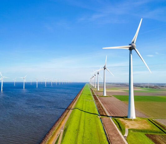 Mehrere Windräder stehen direkt am Meer oder am Strand inmitten der Natur. Hier sieht man einen großen Windpark mit mehreren Windkrafträdern, die Energie aus Windkraft erzeugen.