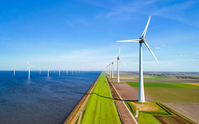 Mehrere Windräder stehen direkt am Meer oder am Strand inmitten der Natur. Hier sieht man einen großen Windpark mit mehreren Windkrafträdern, die Energie aus Windkraft erzeugen.