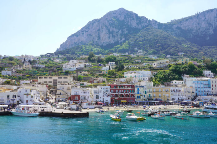 Capri - mitten im Sommer - eine beliebte Urlaubsinsel der deutschen Touristen liegt direkt am Meer. Im Hintergrund liegen hohe Berge und grüne Wälder.