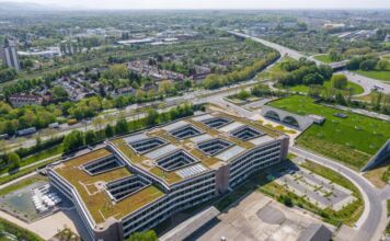 Die Luftaufnahme der Zentrale einer Firma. Großes Gebäude eines Unternehmens in einem Industriegebiet umgeben von Häusern und Industriegebiete sowie Grünflächen.
