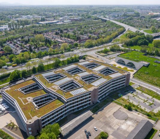 Die Luftaufnahme der Zentrale einer Firma. Großes Gebäude eines Unternehmens in einem Industriegebiet umgeben von Häusern und Industriegebiete sowie Grünflächen.