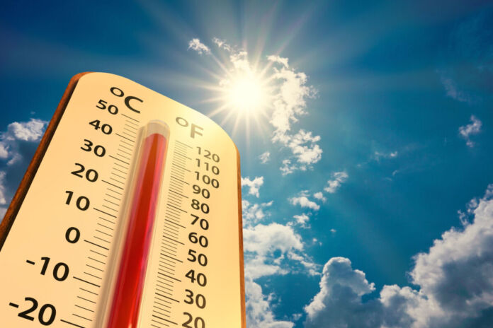 Ein Thermometer in einer Niedrigwinkelansicht. Oben sind ein strahlend blauer Himmel und die Sonne zu erkennen, die herab scheint. Das Thermometer selbst zeigt fast 50 Grad an. Es ist also sehr heißes Wetter.