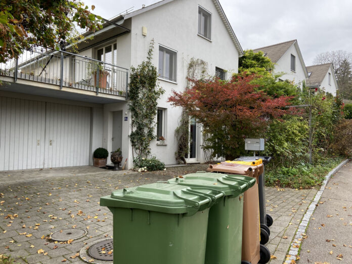 Grüne Mülltonnen sowie eine braune und eine schwarze Tonne stehen an der Straße vor einem Einfamilienhaus mit Garage. Es handelt sich dabei um Biomüll, Plastik und normalen Abfall. In Deutschland gibt es neue Mülltonnen-Regeln.