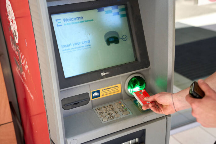 Eine Hand steckt eine Giro-Karte in einen Geldautomaten der Sparkasse, um Geld abzuheben. Auf dem Bildschirm steht in englischer Sprache, dass man seine Karte einstecken soll.