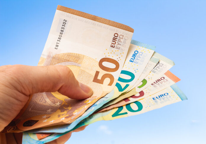 Ein Mann hält mehrere Geldscheine in der Hand, die zu einem Fächer geschoben sind. Man erkennt 50- und 20-Euro-Scheine vor blauem Hintergrund.