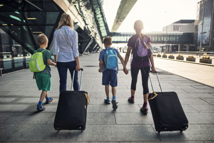 Eine Mutter mit drei Kindern läuft an einem Flughafen entlang. Das Mädchen und die Mutter ziehen jeweils einen Koffer hinter sich her. Alle tragen Rucksäcke. Immer mehr Bürger flüchten ins Ausland.