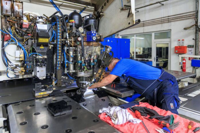 Ein Arbeiter befindet sich in einer Fertigungshalle und bedient eine moderne Maschine. Die Anlage befindet sich in einer Fabrik, in der Produkte für die Industrie hergestellt werden.