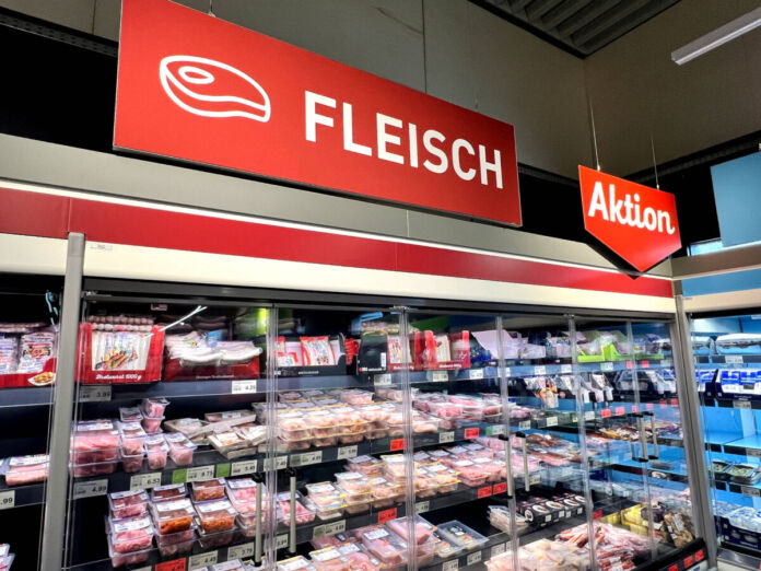 Im Kühlregal eines Supermarktes oder eines Discounters befinden sich viele verschiedene Fleischsorten. Über dem Regal hängt ein rotes Schild mit der weißen Aufschrift "Fleisch". Daneben gibt es ein ebenfalls rotes Schild mit der weißen Aufschrift "Aktion".