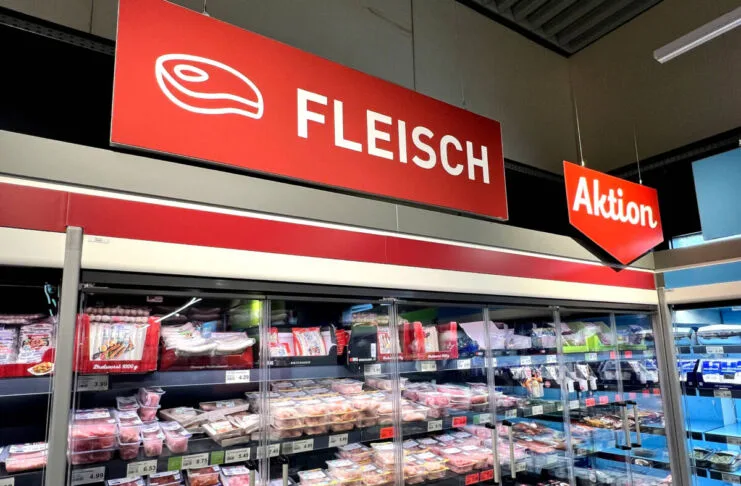 Im Kühlregal eines Supermarktes oder eines Discounters befinden sich viele verschiedene Fleischsorten. Über dem Regal hängt ein rotes Schild mit der weißen Aufschrift "Fleisch". Daneben gibt es ein ebenfalls rotes Schild mit der weißen Aufschrift "Aktion".