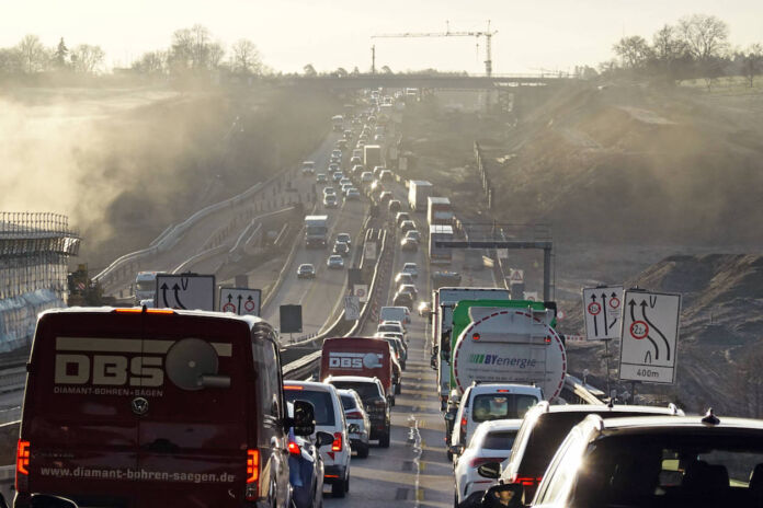 Ein langer Stau auf der Autobahn. Die Autos kommen kaum voran, weil das Verkehrsaufkommen riesig ist, eine Autobahn gesperrt ist und es eine Umleitung gibt. Die Luft ist nebelig, der Verkehr zähfließend.