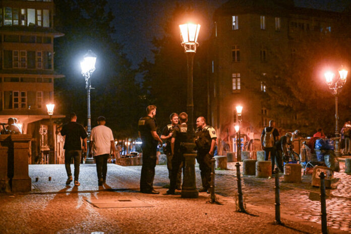 Mehrere Polizisten befinden sich bei einem Einsatz auf der Straße, es ist mitten in der Nacht oder früh am Morgen, die Straßenbeleuchtung ist eingeschaltet. Die Beamten beraten über die Kontrolle von Bürgern oder unbekannten Personen.