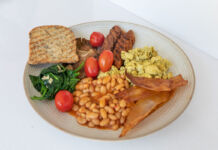 Ein großer Teller, auf dem sich alle Bestandteile für ein abwechslungsreiches Frühstück befinden. Es kann sich auch um ein veganes oder vegetarisches Frühstück handeln, wenn der Speck und das Rührei ebenso vegan sind.