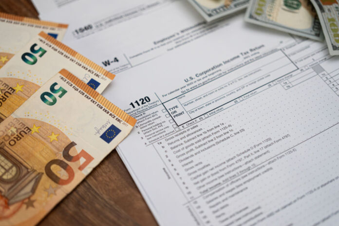 Steuerdokumente und 50-Euro-Scheine auf einem Holzschreibtisch, auf dem das Steuerformular 1120 hervorgehoben ist. Finanzielle Vorbereitung auf die Steuersaison. Konzept der Buchhaltung, Steuererklärung und Finanzverwaltung.