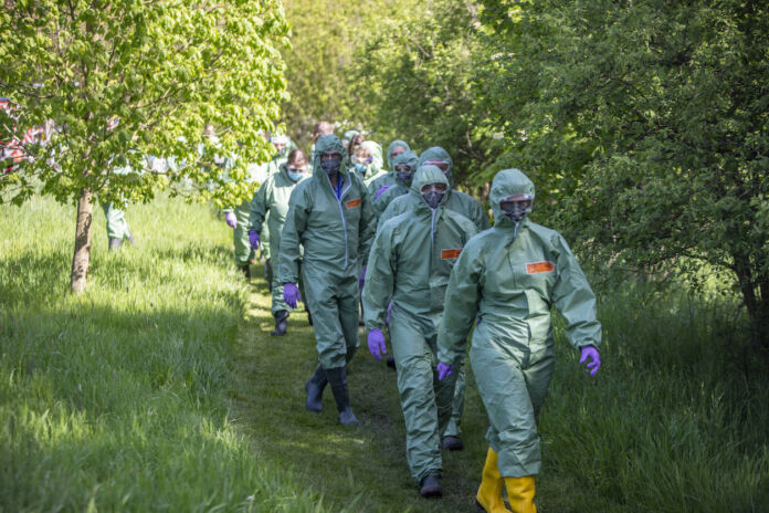 Viele Menschen in Schutzanzügen gegen Infektionen laufen in einer Reihe im Wald. Die grünen Overalls schützen sie vor einem hochansteckenden Virus, der sich gerade in einem Bundesland Deutschlands ausbreitet.
