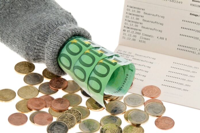 Neben einem Kontoauszug liegen zahlreichen Cent-Münzen sowie Hundert Euro Scheine, die in einen grauen Strumpf gewickelt worden sind. Der klassische Sparstrumpf dient mit der Sparsumme für große Ausgaben und Anschaffung sowie zur finanziellen Sicherheit.