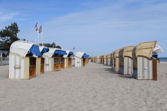 An einem Strand am Meer stehen mehrere Reihen von Strandkörben für die Touristen und Urlauber bereit. Der Himmel ist strahlend blau. Es scheint Sommer zu sein.