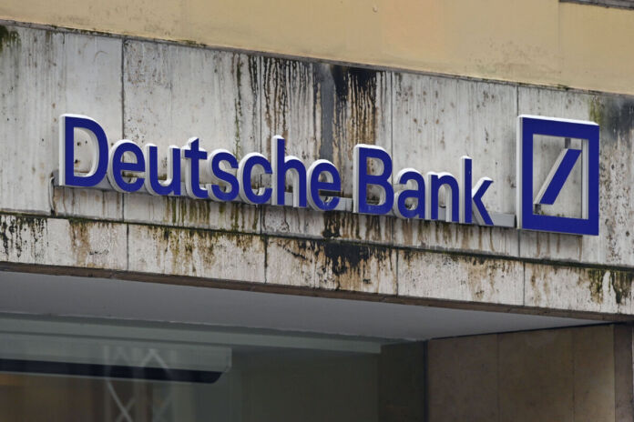 Der Schriftzug der Deutschen Bank, das blau-weiße Logo des Konzerns, hängt an einer Hausfassade, die an Farbe verliert und wo der Putz bereits bröckelt.