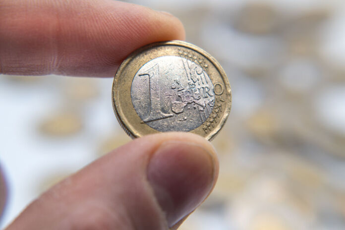 Die Hand eines Mannes hält eine 1-Euro-Münze direkt in die Kamera. Sie scheint schon etwas abgegriffen zu sein.