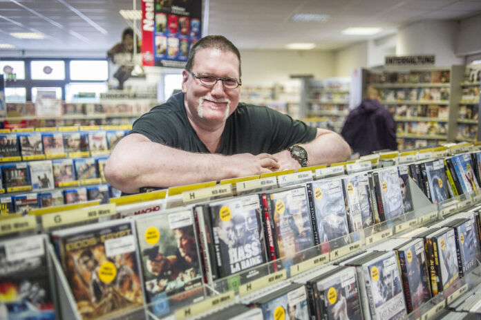 Der Betreiber einer Videothek nimmt die Regale ab. In den Regalen stehen DVDs und Videos von verschiedenen Filmen und John wird. Hier kann man Komödien, Thriller, Krimis, Kinofilme und Kunstfilme ausleihen. Dafür zahlt man eine Leihgebühr.
