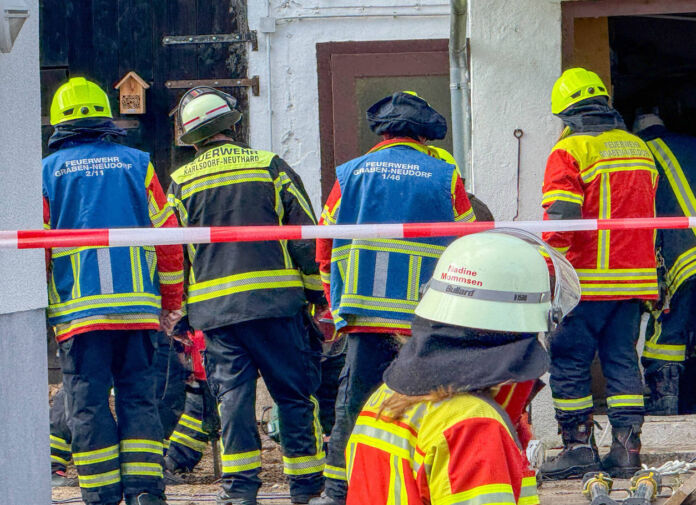 Unzählige Einsatzkräfte der Feuerwehr stehen in voller Montur hinter einem Absperrband bei einem Großeinsatz in der Nähe von Karlsruhe. Sie versuchen bei der Rettungs-Aktion etwas aus einem Brunnenrohr zu befreien.