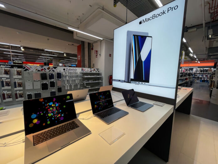 Mehrere MacBooks stehen in einem Saturn zum Verkauf. Im Hintergrund sieht man eine große Apple-Werbung für das neuste MacBook Pro.
