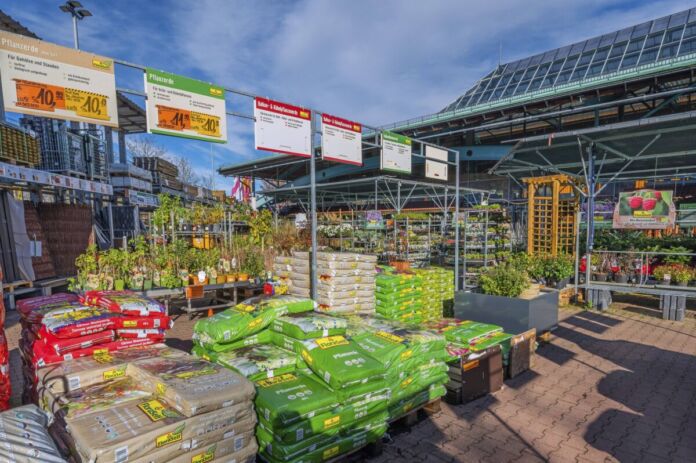 Das Foto zeigt die Außenabteilung eines Baumarktes. Dort stehen zahlreiche Produkte zur Auswahl, unter anderem sieht man mehrere Säcke, in denen sich wohl Erde befindet.