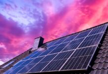 Blick auf das Dach eines Hauses. Auf dem Dach sind thermische Solarkollektoren angebracht. Der Himmel über dem Dach des Hauses leuchtet auffällig in einer lila-pinken Farbe.